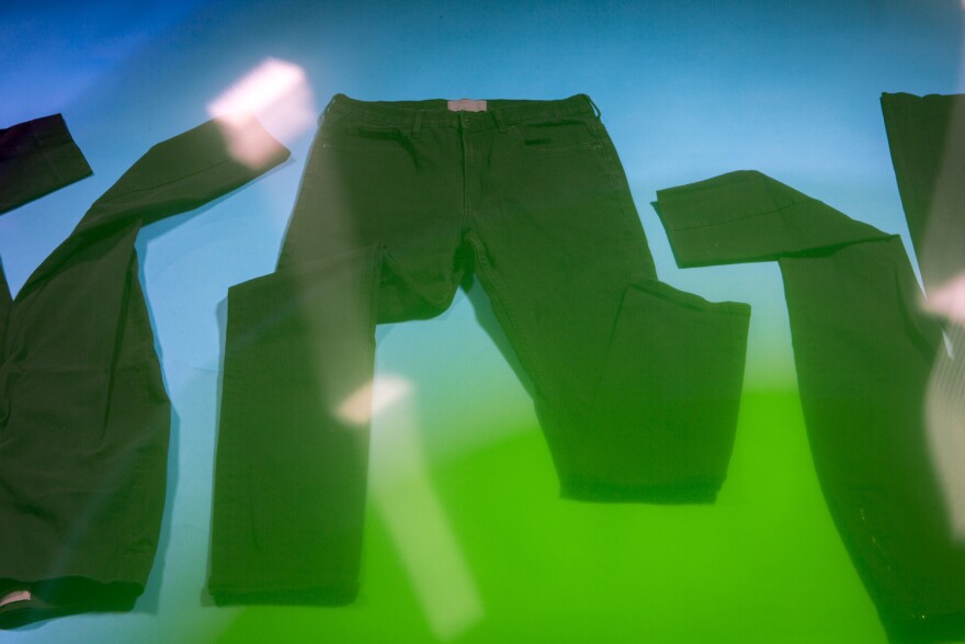 Three pairs of black pants are arranged topsy turvy on a blue backdrop with a green gradient coming over them from the bottom right corner of the frame.