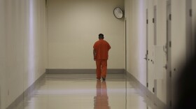 A person in an orange jumpsuit walks down a white hallway.