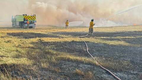 Firefighters extinguish a blaze at a hay field in the Eagle River area
