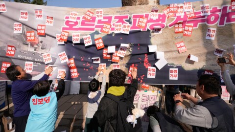 South Korean protesters attach stickers on a banner showing the Strait of Hormuz during a rally against the U.S. and Israel attacks on Iran near the presidential office in Seoul, South Korea, Saturday, March 28, 2026. The letters read "Refuse sending troops to Hormuz!" (AP Photo/Ahn Young-joon)