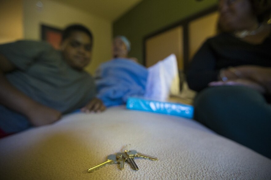 After months of moving from hotel to hotel while applying for more permanent housing Lisbeth Sandoval, (far right), her daughter, Sheylibeth, (center) and her son, Stephen, sit next to the keys to their new apartment. (Jesse Costa/WBUR)