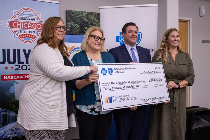 Four people hold a giant check that details $30,000 are going to the McLean County Center for Human Services from the NASCAR Foundation and Blue Cross Blue Shield of Illinois.