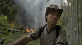 Martins, a settler in the Amazon, perched on his motorbike as the forest burns behind him in this still from The Territory