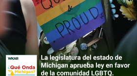 En la imagen se puede observar una bandera arcoiris del orgullo LGBTQ y una pancarta que dice en ingles: "Cuir y Orgulloso". En el lado inferior de la imagen esta el logo de Que Onda Michigan sobre un fondo blanco. En la parte derecha las siguientes palabras estan escritas: "La legislatura del estado de Michigan aprueba ley en favor de la comunidad LGBTQ." En el lado superior de la imagen se encuentra las pablaras "WKAR" en color blanco.  y "Episodio 84".