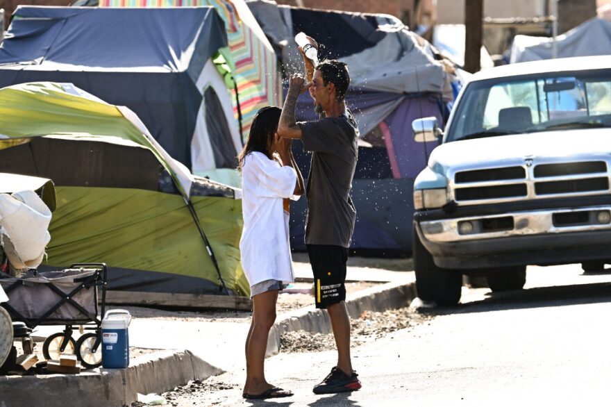 Roni and John pour water on themselves to cool off from extreme heat while residing in "The Zone," a vast homeless encampment where hundreds of people reside, during a record heat wave in Phoenix, Arizona. (Photo by PATRICK T. FALLON/AFP via Getty Images)