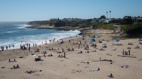 An overview of Natural Bridges State Beach from the upper parking lot shows people lounging on the beach and in the water.
