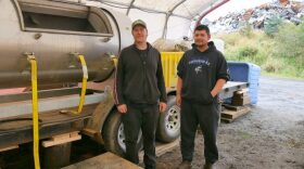 Brandon Thynes, Petersburg Indian Association’s Tribal Resource Director, and his assistant, Clifton Gudgel, stand next to the tribe’s new composting machine, which is housed in a portable building at the Petersburg Borough’s baler facility. (Photo by Angela Denning/KFSK)