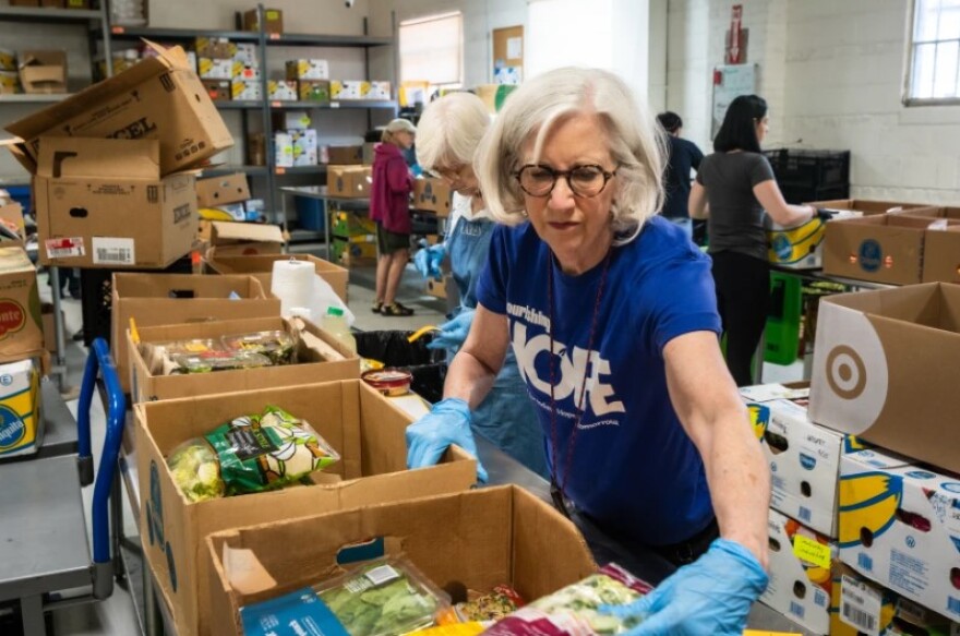 Susan Matthews, wearing thicker circular glasses with shoulder length, wavy white hair, intently sorts produce June 16 2025 during her volunteer shift at Nourishing Hope, 5151 N. Ravenswood Ave. in Chicago