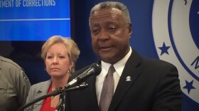 Jackson County Executive Frank White stands at a podium with the Jackson County seal on the wall behind him and to the right and an unidentified woman to the left.