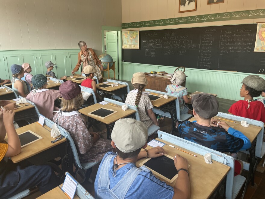 Children listening to a teacher in a old fashioned one-room school house