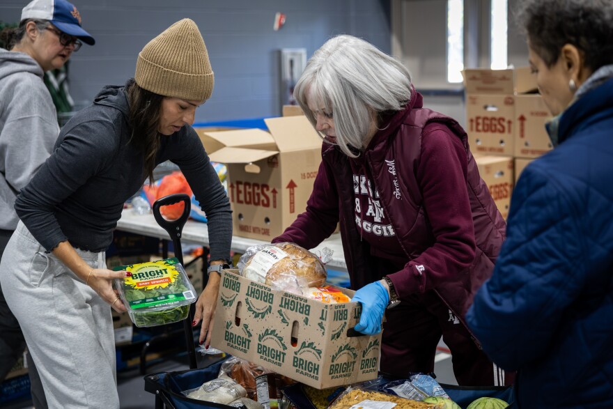 Volunteers Brooke Marshall, left, and Gwynn Beeler, center, help load up groceries for an attendee of the Central Texas Food Bank food distribution on Tuesday, Nov. 11, 2025, at George Morales Dove Springs Recreation Center in Austin. Food bank staff reported a 50% surge in demand at food distributions as SNAP benefits are cut. Michael Minasi / KUT News