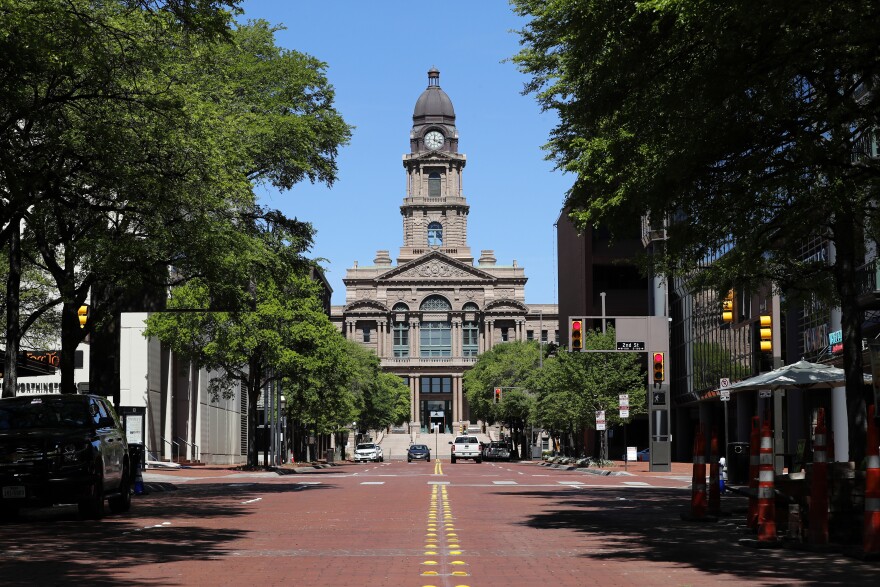 A photo of Tarrant County's historic downtown courthouse, a brown stone building with a tall clocktower. The photo is taken from the middle of Main Street looking down, a red brick road lined with buildings.
