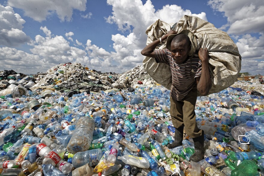 A man walks on a mountain of plastic bottles as he carries a sack of them to be sold for recycling after weighing them at the dump in the Dandora slum of Nairobi, Kenya, on Dec. 5, 2018.