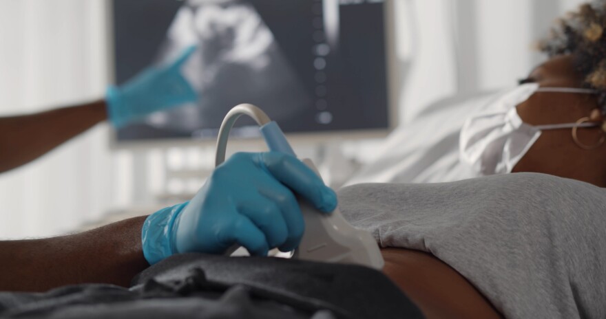 Close up of afro doctor examining patient pregnant woman with scanner. Afro-american pregnant woman in protective mask undergoing ultrasound test at gynecologist office