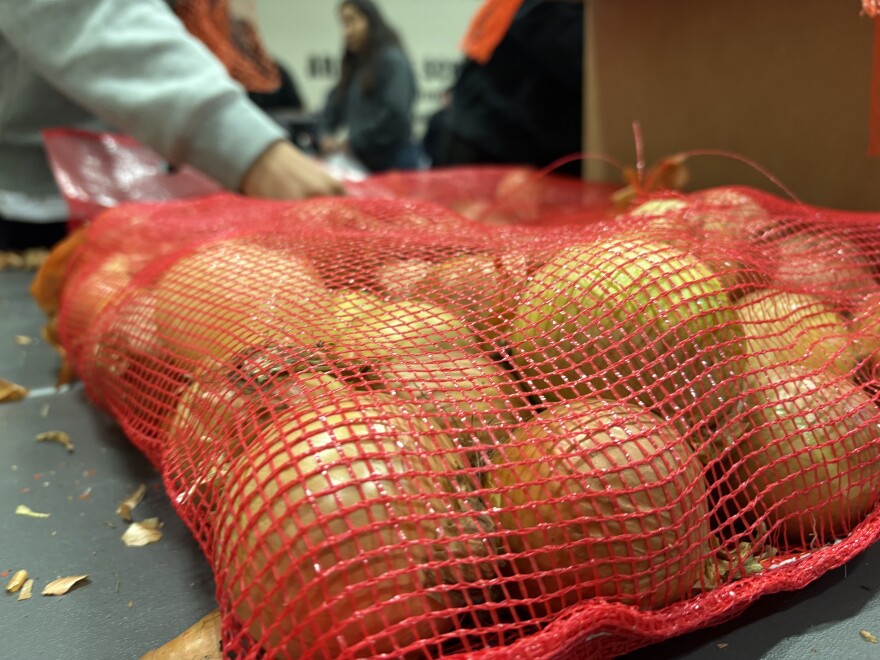 A mesh bag of yellow onions, getting sorted by volunteers in the background.