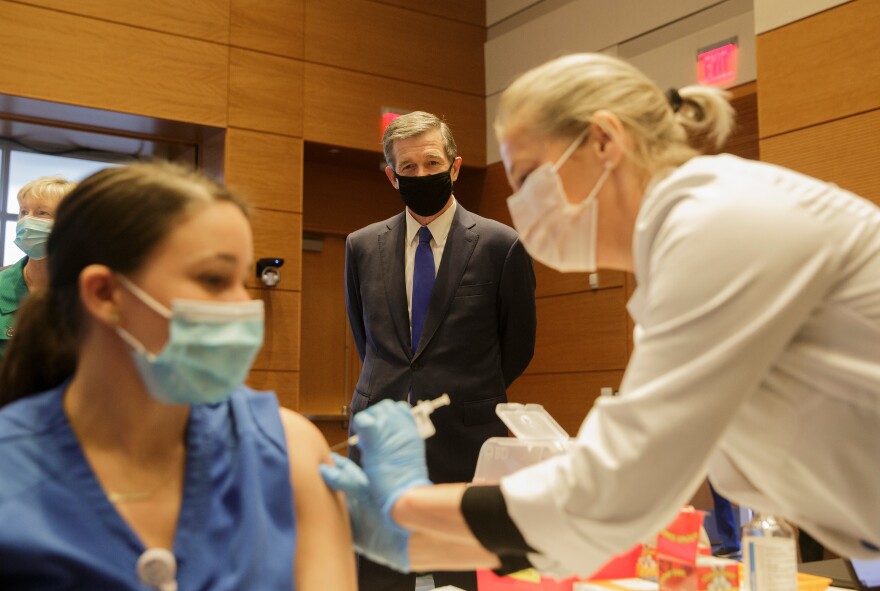 Gov. Roy Cooper watches while Tracy Toner gives a COVID-19 vaccination to Duke nurse Arianna Motsinger at the Duke University School of Medicine in Durham on Monday, December 21, 2020.