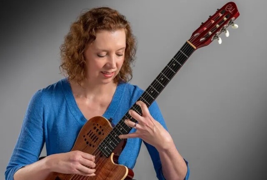 A woman in a blue sweater looks down at her hands while playing guitar.