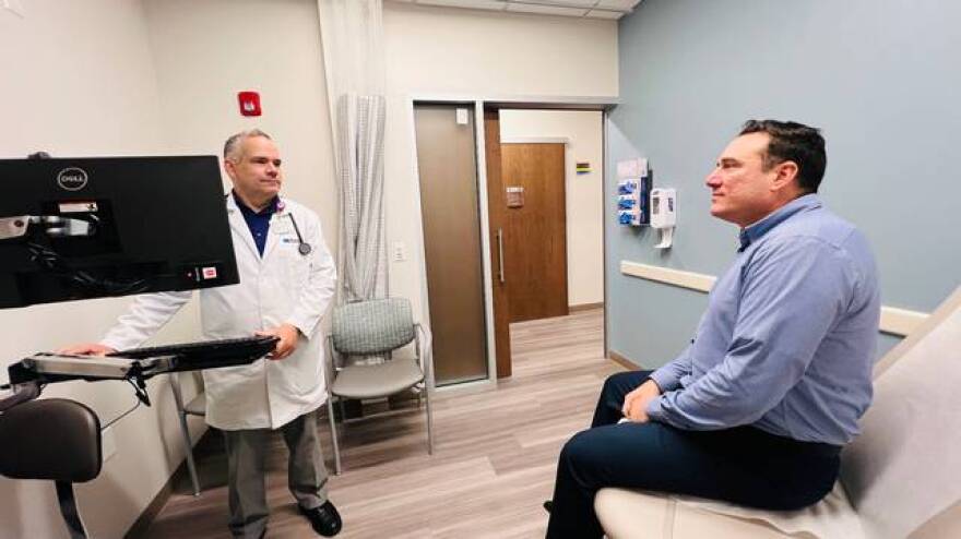 Doctor stands at a computer across from a man sitting down who is patient