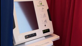 Electronic voting machine with a blank screen surrounded by a blue curtain on the left and a red curtain on the right. 