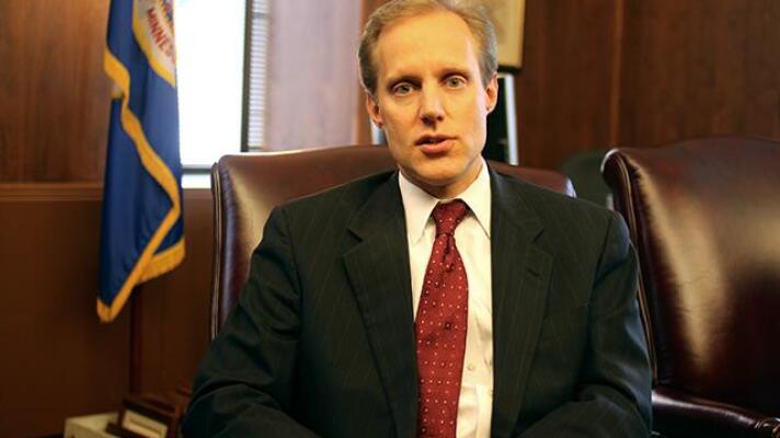  Minn. Secretary of State Steve Simon at a desk, in front of Minnesota flag.