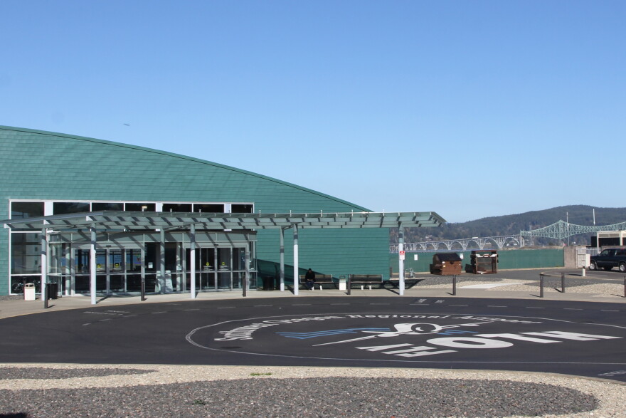 An airport terminal building overlooks a bay with a cantilever bridge in the background and a painted parking lot in the foreground with "Fly OTH" pained on it.