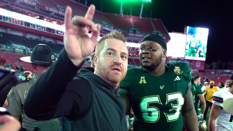 A football coach wearing a green shirt looking ahead with a football player in a 63 green jersey behind him