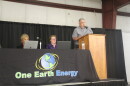 A business executive speaks at a podium next to a table set up for a public meeting. 