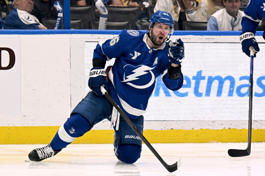 Hockey player in a blue uniform with a lightning bolt on the front with his knee on the ice and fist in the air celebrating