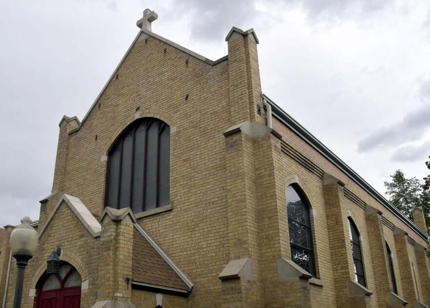 Exterior shot of a tan bricked church with red doors.