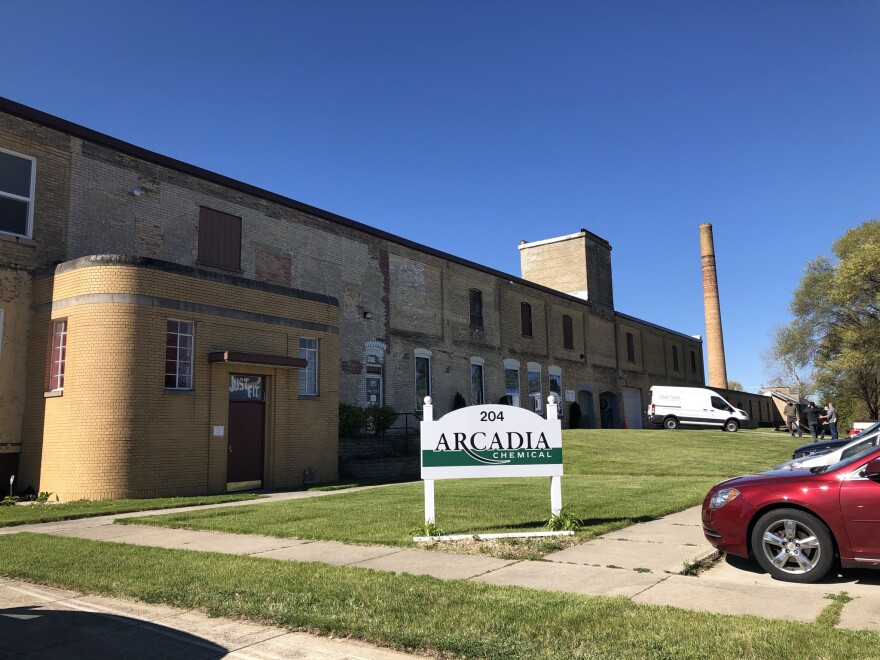 Wide view of a long, mostly two-story brick building with Art Deco entrance. Cars are parked in a lot in front of the building.