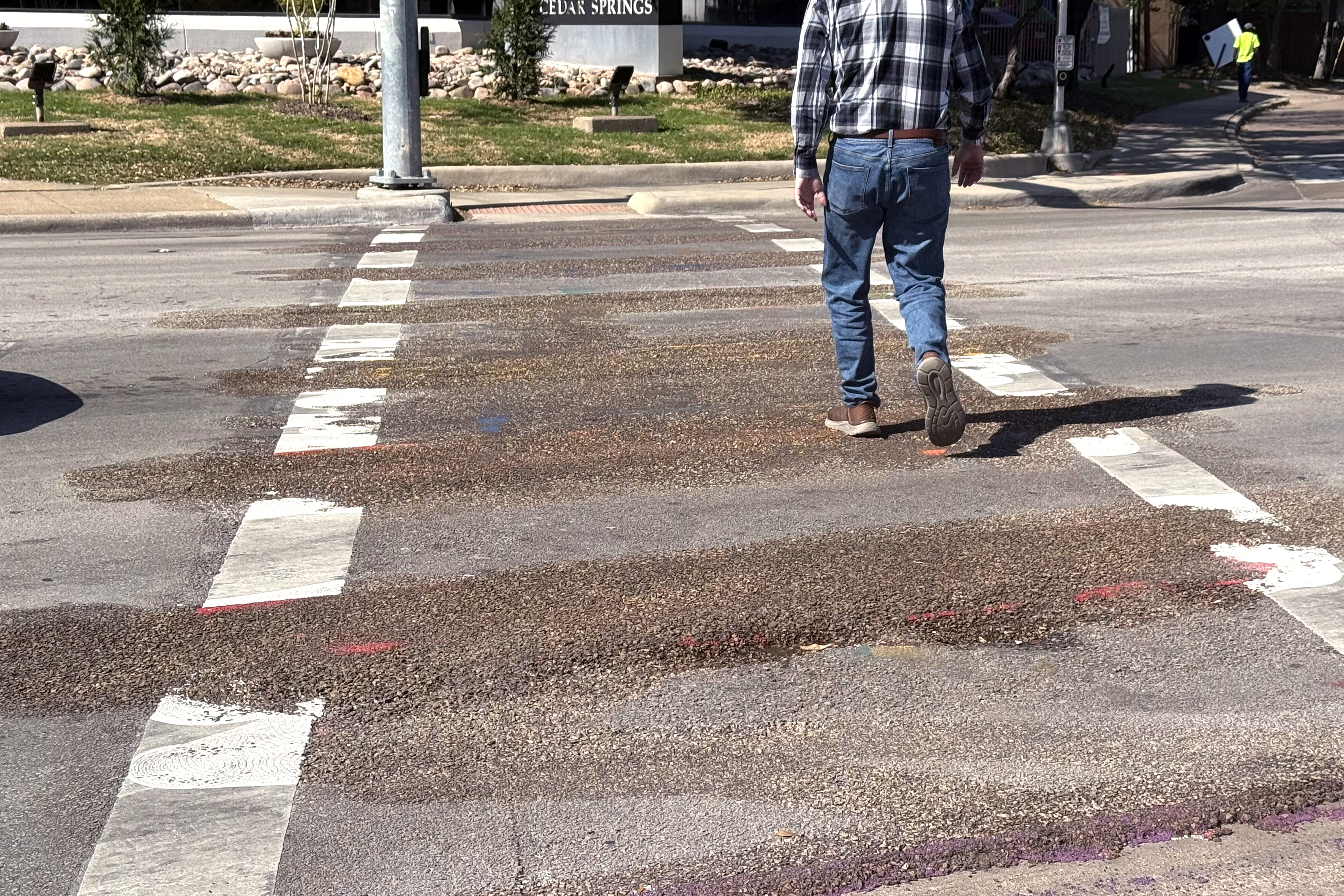 Man walks across wet intersection in Oak Lawn Dallas after city crews removed rainbow crosswalk markings under Texas state mandate